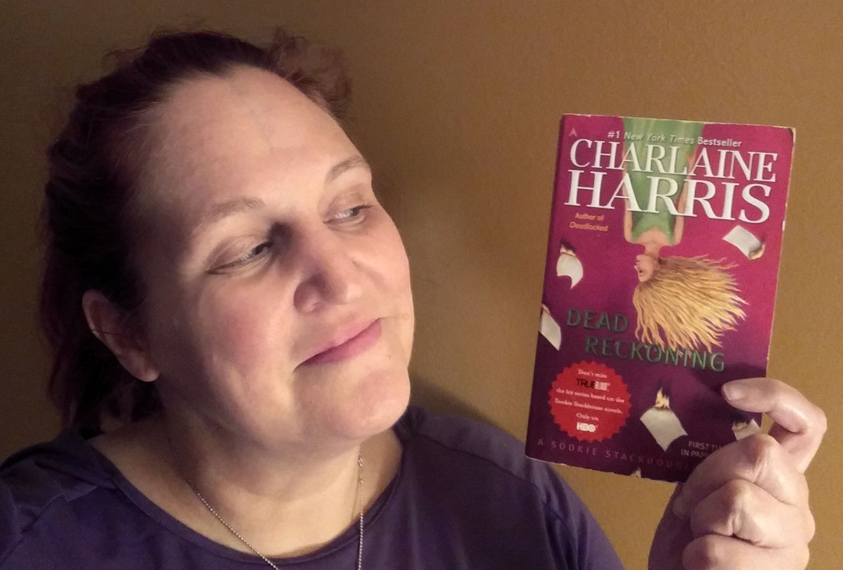 Carma holding a copy of Dead Reckoning by Charlaine Harris