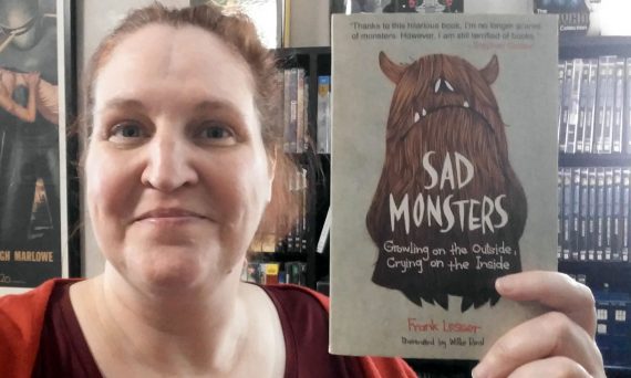 Carma Spence holding a copy of Sad Monsters by Frank Lesser